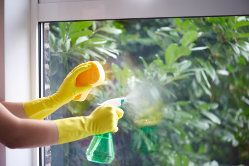Woman wearing yellow washing up gloves to use spray bottle and sponge to clean window